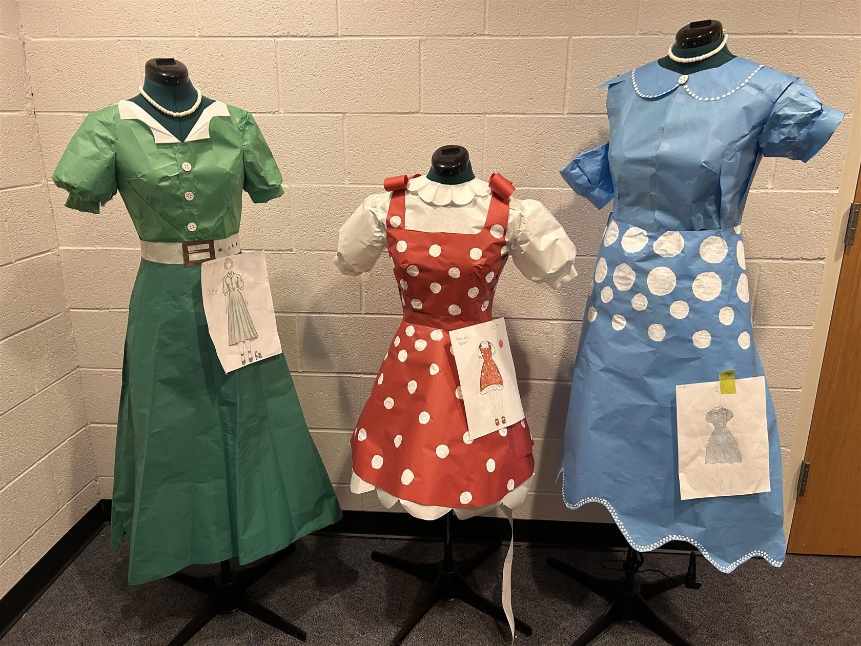 Three dresses created by students out of paper are on mannequins. 