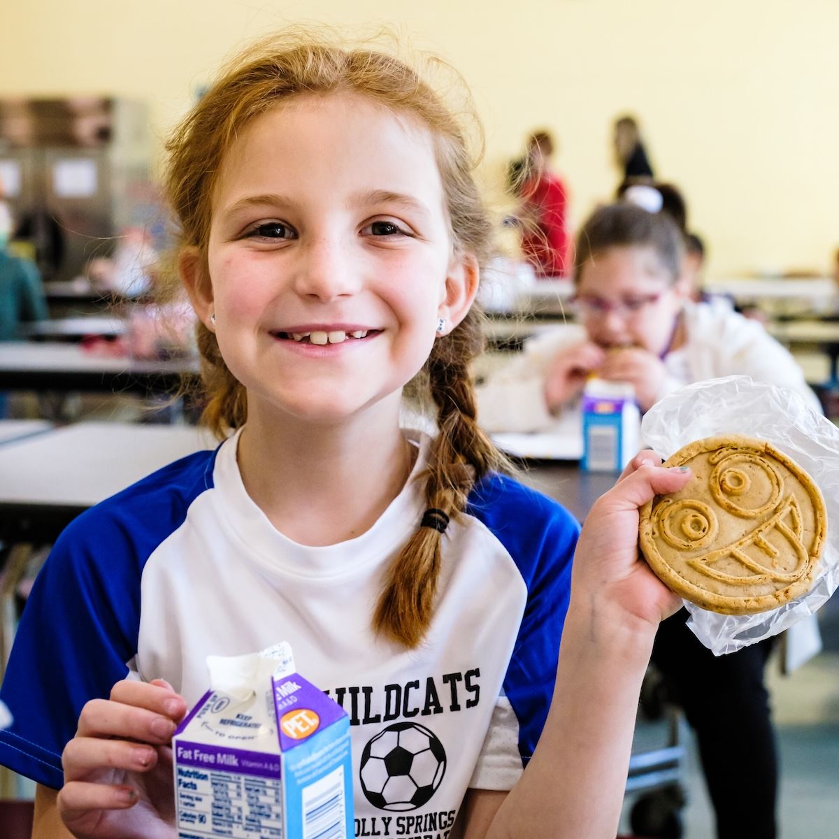  A young student smiles while holding up a pancake in the shape of a smiley face