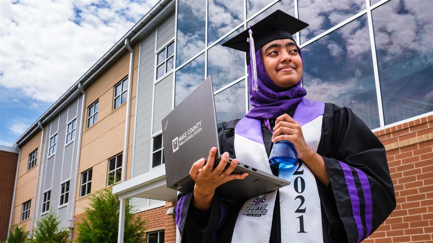 student outside holding laptop wearing a cap and gown