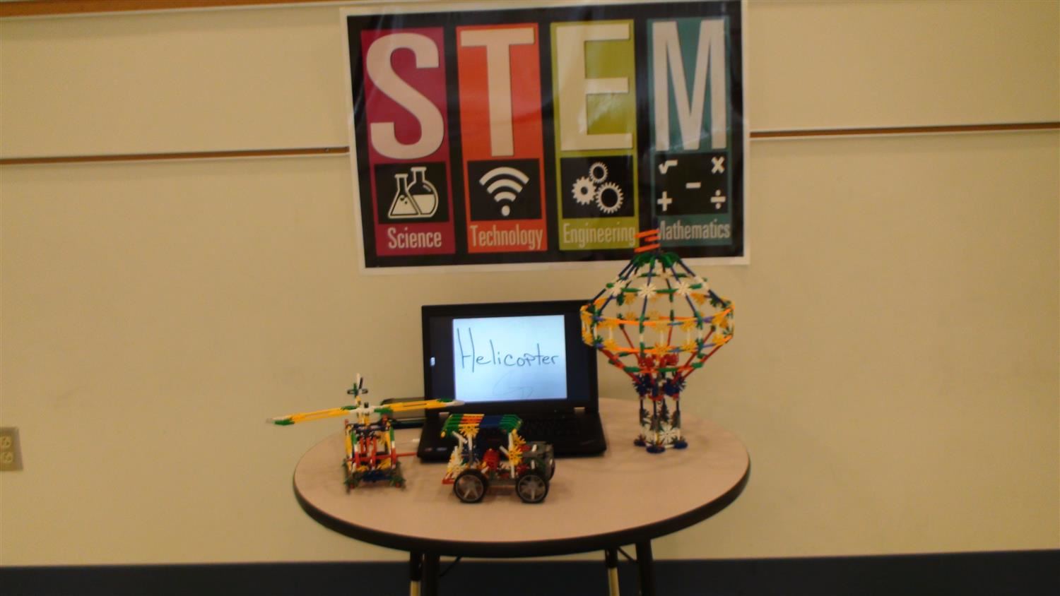 STEM sign with laptop that reads, "helicopter" and three models of vehicles built with K'nex build pieces