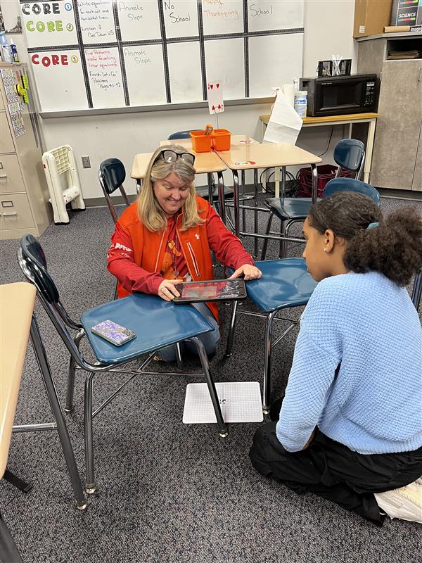 Teacher is on the floor kneeling infront of a student, both are looking at stop motion video on the Ipad